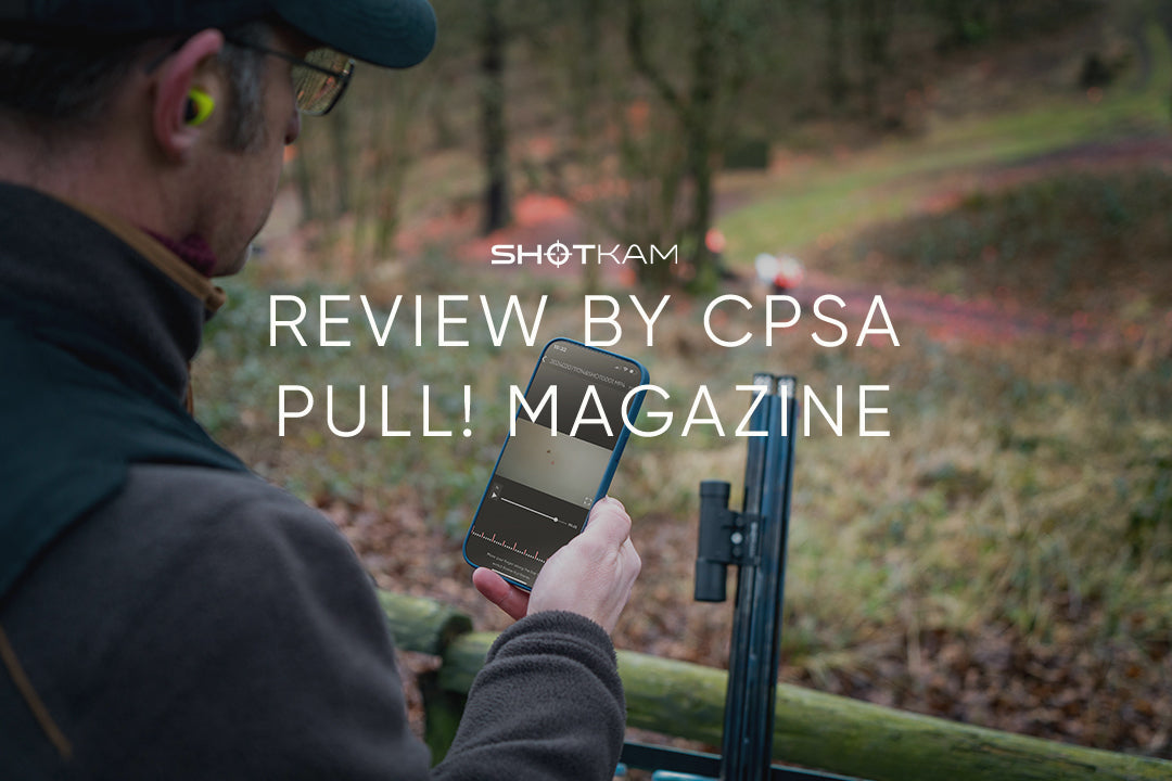 European shooter analyzing ShotKam video footage on a smartphone in a forest setting, featured in CPSA's PULL! Magazine. Ideal for refining clay shooting accuracy.