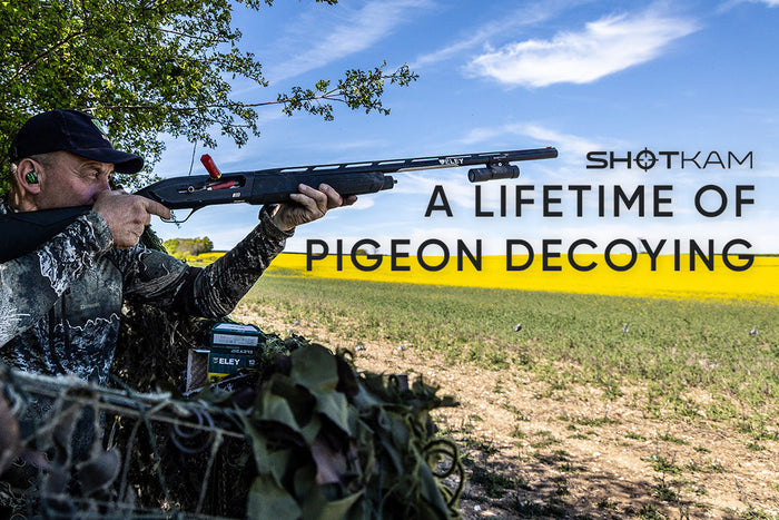 Hunter aiming a shotgun from a camouflage hide overlooking farmland with the title "A Lifetime of Pigeon Decoying" and ShotKam logo.