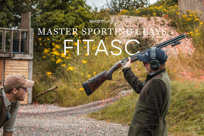 Two clay shooters sharing a moment during a FITASC round; one raising his shotgun with a ShotKam attached.